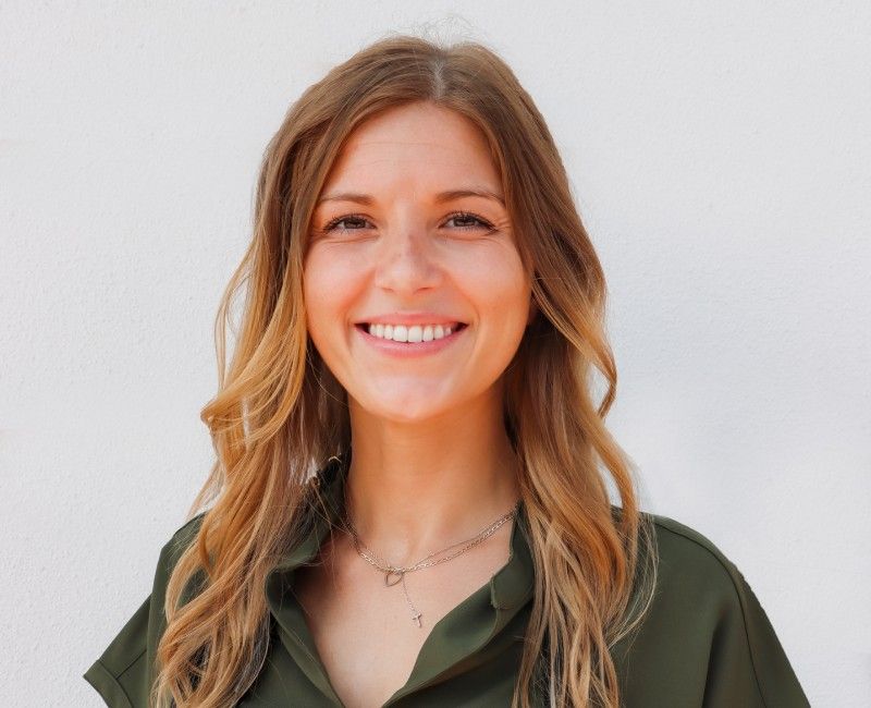 Smiling woman with long hair wearing a green shirt, looking directly at the camera.