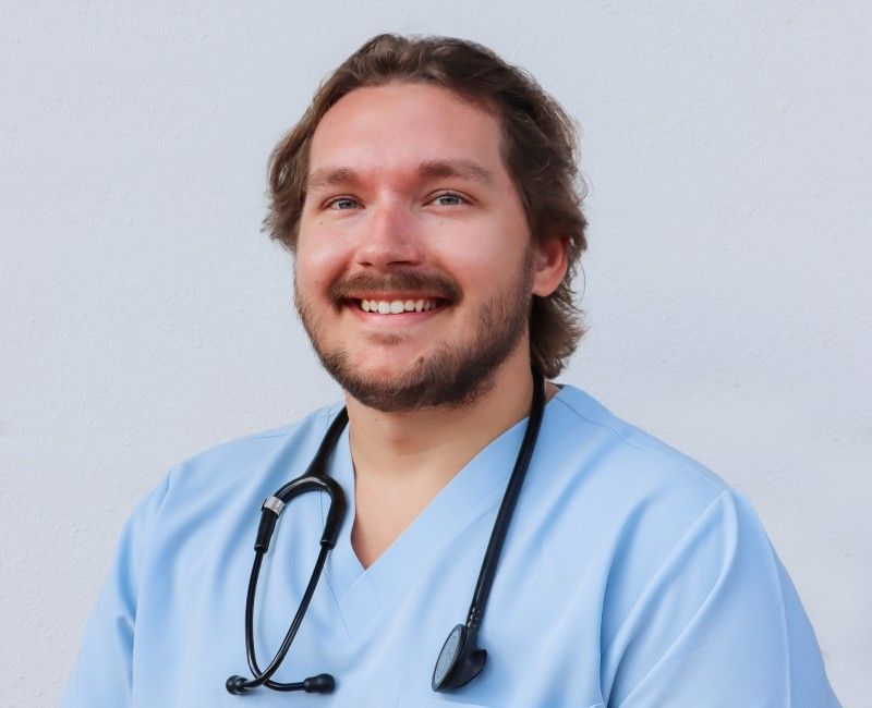 Smiling person in light blue scrubs with a stethoscope around their neck.