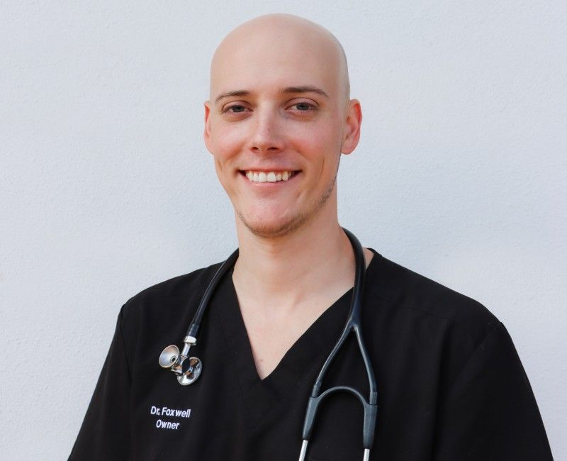 A smiling person wearing a black scrub top with a stethoscope around their neck.