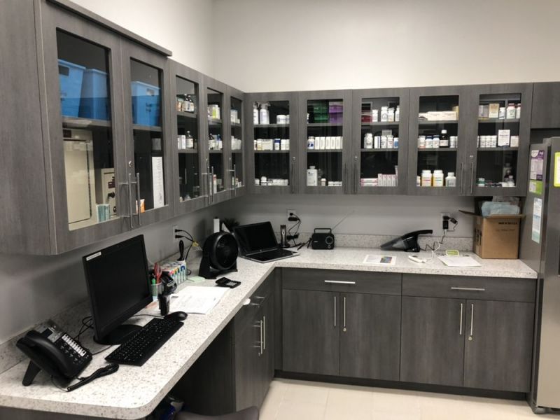 A modern pharmacy workspace with gray cabinets, computer, phone, and various medications on display.