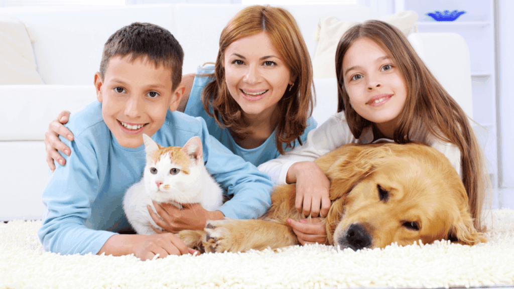 A family posing with a cat and a golden retriever on a carpet, all smiling warmly.